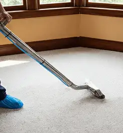 Steam carpet cleaning technician using a hot-water extraction wand on a residential carpet, wearing blue protective shoe covers Bakersfield, CA.
